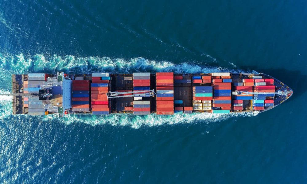 Aerial view Top speed with beautiful wave of container ship full load container with crane loading container for logistics import  export or transportation concept background.